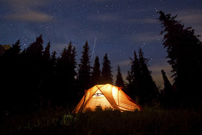 stars above the mountains with tent highlighted by lamp and trees on background
