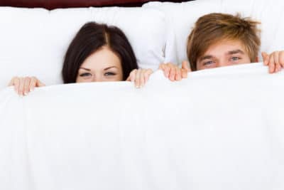 happy young couple in bed "young lovely couple lying in a bed, happy smile looking at camera, cover under blanket top angle view up above"
