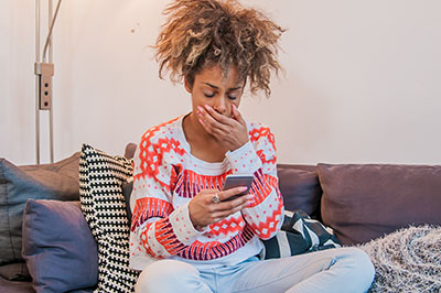 Young African woman sitting in her living room and texting. Tired and sleepy black woman yawning