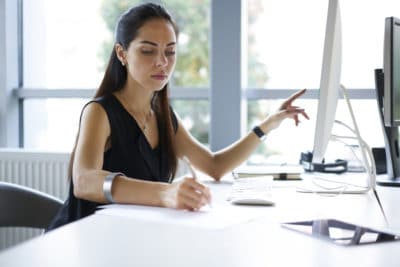 Concentrated professional female journalist making research browsing information for article using computer and wireless connection in office, businesswoman counting profit of company doing report