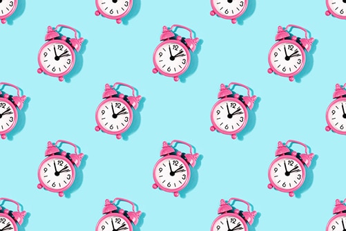 Seamless pattern made with vintage pink alarm clock on turquoise background. Flat lay, top view.