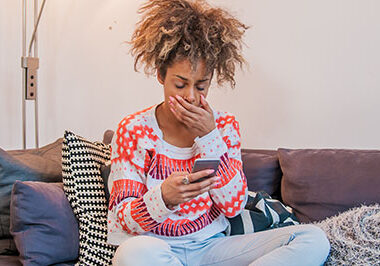 Young African woman sitting in her living room and texting. Tired and sleepy black woman yawning